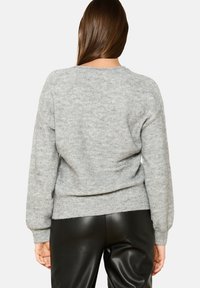 Grauer Strickpullover mit rundem Ausschnitt, geripptem Saum und Bündchen sowie strukturierter Oberfläche. Kombiniert mit schwarzen Kunstlederhosen.