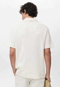 Camisa blanca de manga corta con cuello clásico, tejido texturizado y corte recto, mostrada desde la parte de atrás.