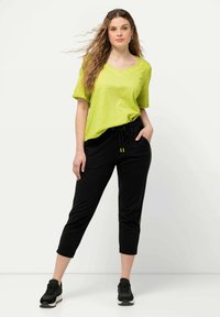 Limoengroene V-hals T-shirt met korte mouwen, gecombineerd met zwarte cropped joggers met gele zijstrepen en een elastische tailleband.