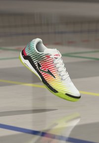 White athletic shoe with gradient design in green, yellow, orange, and red. Features black accents, a textured sole, and prominent brand logo.