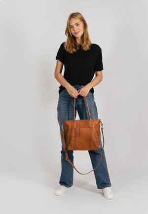 Tote-Bag aus tanfarbenem Leder mit zwei Griffen und verstellbarem Schulterriemen. Glatte Textur, rechteckige Form und minimalistisches Design.