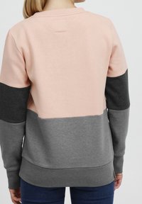 Sudadera con bloques de color en rosa claro, gris oscuro y gris medio. Tejido suave, cuello redondo y puños acanalados. Diseño simple con una etiqueta en la parte posterior.