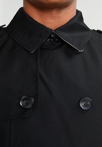 Czarny płaszcz trench z wysokim kołnierzem, podwójnym zapięciem na guziki i błyszczącymi guzikami. Gładki materiał z delikatnym połyskiem, elegancki design.