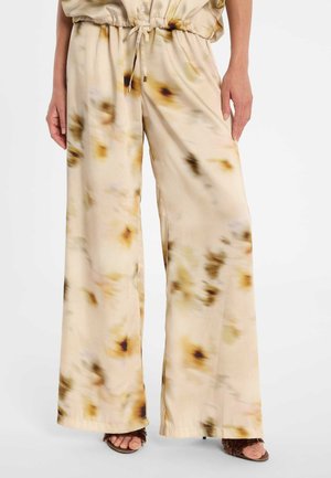 Beige Hosen mit weitem Bein, braun-schwarzem abstraktem Blumenmuster, Kordelzug am Bund, getragen mit braunen Sandaletten mit offenem Zehenbereich und Absatz.