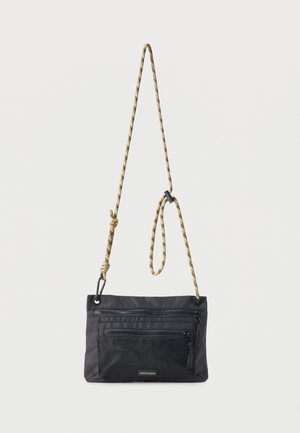 Bolso bandolera negro con bolsillo frontal de malla con cremallera y correa de cuerda ajustable con patrón negro y marrón claro.