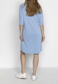 Světlomodré šaty s krátkým rukávem a uvolněným střihem, do kolen, vyrobené z hladkého materiálu. Nosené se bílými teniskami. Jednoduchý, minimalistický design.