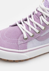 Zapatilla alta de ante morado con cordones blancos, ojales de metal y acentos en morado claro. Presenta una suela de goma con agarre texturizado.