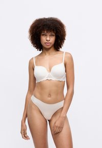 Sujetador beige claro con encaje y tirantes ajustables, combinado con un tanga sin costuras a juego. Tejido suave, textura agradable y diseño minimalista.