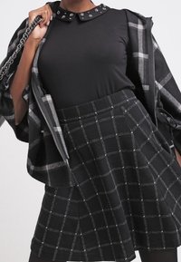 Black long-sleeve top with a collar embellished with studs, paired with a plaid skirt featuring a textured fabric in black and gray tones.