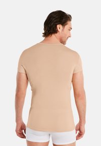 Beige fitted t-shirt with short sleeves, soft fabric, round neckline, and a seamless back design. Worn by a man facing away from the camera.