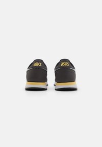 Black athletic shoes with yellow ASICS logo, white and yellow midsole, and textured fabric upper. Rounded heel with minimal design details.