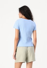 Lys blå ribbestrikket topp med korte ermer, med bølgekant og teksturdetaljer, kombinert med lysegrønne shorts.