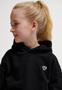 Svart hoodie med en stor huva, med en liten vit broderad logotyp på bröstet. Mjuk tyg, avslappnad passform och långa ärmar.