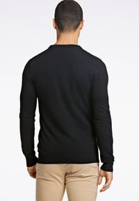 Maglione nero in maglia con maniche lunghe e scollo rotondo, caratterizzato da una vestibilità aderente e polsini e orlo a coste. Texture liscia su tutta la superficie.