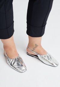 Silberne metallische Slingback-Schuhe mit quadratischer Zehenpartie, gefältetem Oberdesign, flacher Sohle und minimalen schwarzen Akzenten. Geeignet für den lässigen Gebrauch.