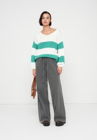 Pull en tricot rayé blanc et turquoise, manches larges, associé à un pantalon taille haute gris à jambes larges et des chaussures plateformes noires.