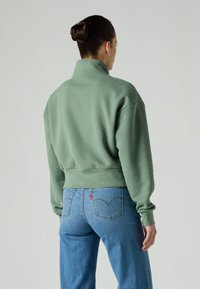 Sweat-shirt vert court avec un col montant, un ourlet côtelé et des épaules tombantes, associé à un jean bleu clair à jambes droites.