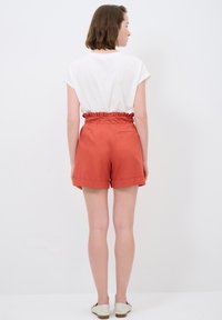 Pantaloni corti rossi con vita arricciata e tasca posteriore, abbinati a una camicia bianca a maniche corte. Tessuto morbido e vestibilità casual.