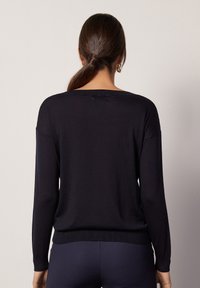 Granatowy sweter z długim rękawem o luźnym kroju, miękkiej dzianinowej fakturze i prążkowanym wykończeniu. Posiada szeroki dekolt i opadające szwy ramion.