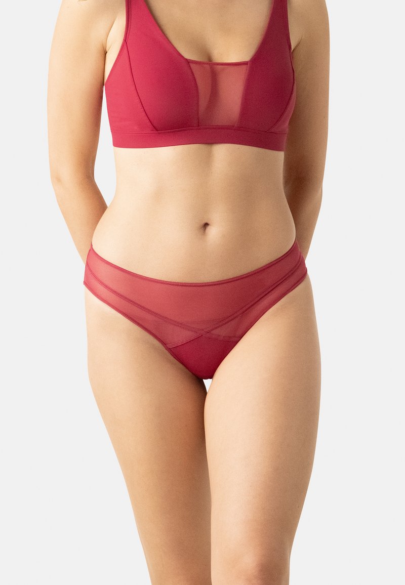 Ensemble de lingerie rouge comprenant un soutien-gorge en maille transparente à décolleté plongeant et un slip assorti avec des accents transparents, les deux pièces ayant une texture de tissu lisse.
