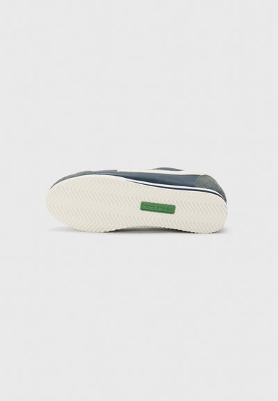 Adidași albastre cu un superior texturat de culoare bleumarin, detalii albe și logo verde. Prezintă o talpă din cauciuc crem cu un model de zimți.