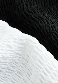 Dos piezas de tela: una negra y una blanca, ambas con un diseño texturizado y fruncido con costuras elásticas visibles.