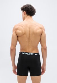 Πλάγια όψη άνδρα χωρίς μπλούζα που φοράει μαύρα εσώρουχα boxer της Nike, με φόντο απλό φωτεινό χρώμα.