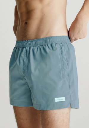 Costumi da bagno da uomo in azzurro chiaro, realizzati in tessuto morbido con vita elastica, dotati di una tasca laterale e di un piccolo etichetta con logo.