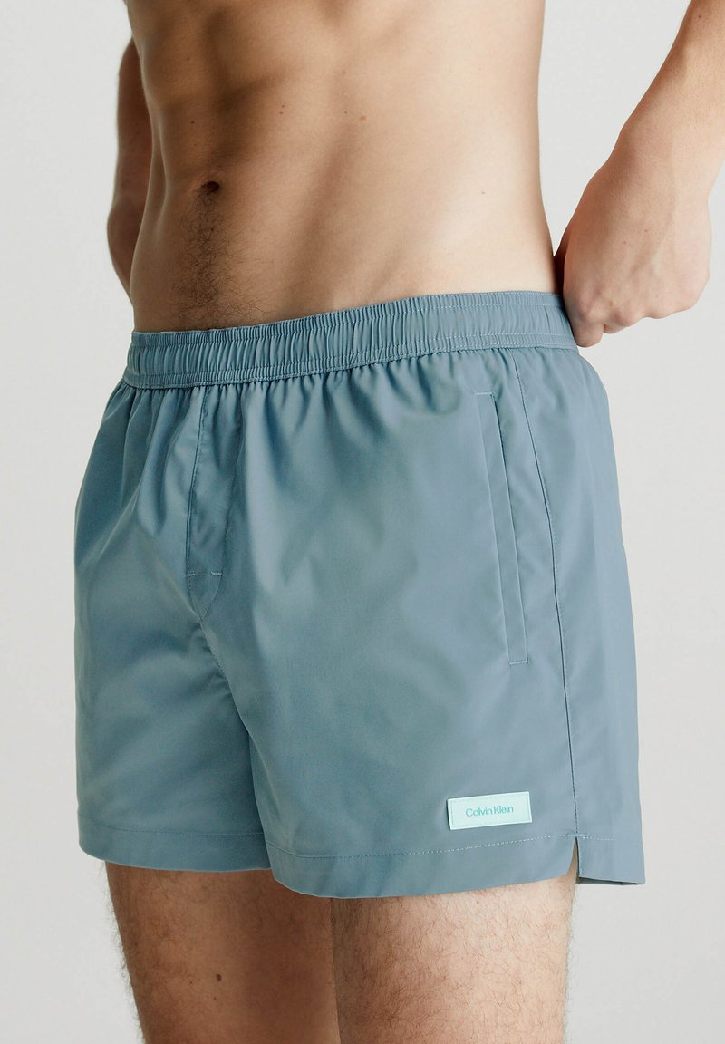 Costumi da bagno da uomo in azzurro chiaro, realizzati in tessuto morbido con vita elastica, dotati di una tasca laterale e di un piccolo etichetta con logo.
