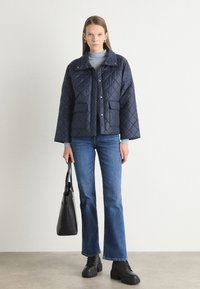 Κουβερτισμένο ναυτικό σακάκι με γιακά, κουμπιά σνέπ και δύο μπροστινές τσέ�πες. Συνδυασμένο με ίσιες μπλε τζιν παντελόνες και μαύρες χοντρές μπότες.