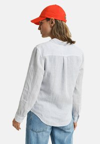  Lichtblauw en wit gestreepte lange mouwen shirt met een ronde onderkant en een achter yoke-detail, gecombineerd met een oranje honkbalpet.