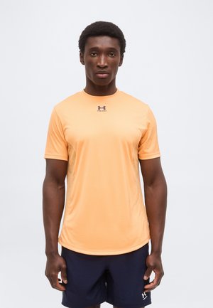 Homme portant un t-shirt pêche à manches courtes Under Armour et un short bleu marine, debout devant un fond clair uni.