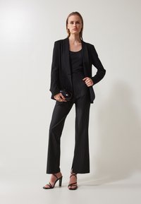 Svart blazer over en svart tank topp, sammen med svart og hvit stripete høy midje bukser og svart hæl-sandaler. Rund svart håndveske.