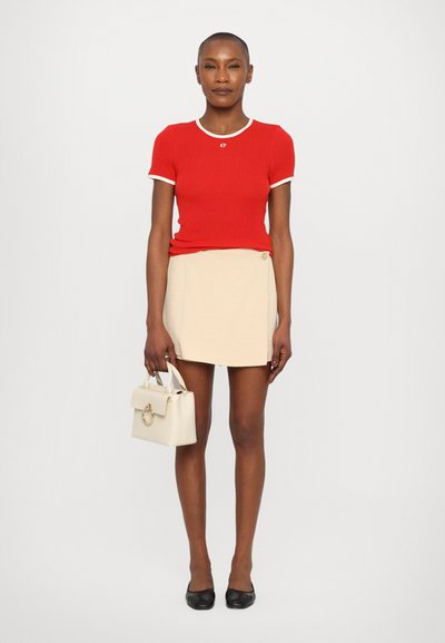 Haut à manches courtes rouge à côtes avec un bord blanc, associé à une mini-jupe beige. Tient un petit sac à main crème. Ballerines noires aux pieds.
