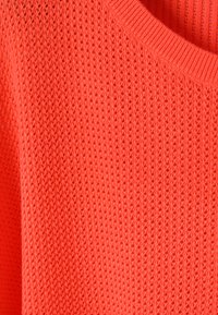 Pull en tricot orange vif avec un motif texturé et un col rond côtelé, présenté en vue rapprochée.