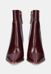 Botas de tobillo de cuero burdeos con un acabado brillante, puntera afilada y cremalleras laterales. Presentan una forma esbelta y cónica con una textura suave.