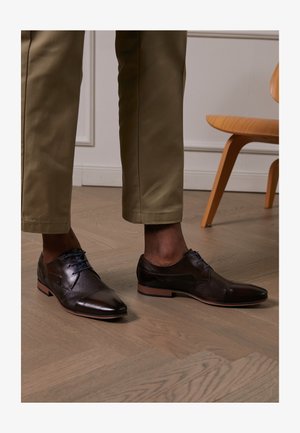 Zapatos de vestir de cuero marrón con un acabado liso y detalles texturizados, con cordones azules y un diseño de punta afilada.