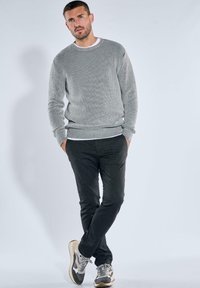 Grau geripptes Sweatshirt mit Rundhalsausschnitt, kombiniert mit dunkelgrauen Slim-Fit-Hosen und mehrfarbigen Turnschuhen. Das Model posiert vor einem hellen Hintergrund.
