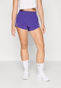 Lila Sport Shorts mit einem breiten Bund, Taschen an den Seiten und einem kontrastierenden weißen Logo. Leichter Stoff mit einer glatten Textur.