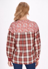 Camicia a quadri con una parte superiore floreale rossa, caratterizzata da maniche lunghe, vestibilità comoda e orli a polsino. Il tessuto è morbido e testurizzato.