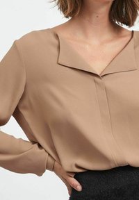Blusa beige con scollatura a V, maniche lunghe e vestibilità ampia. Realizzata in tessuto leggero con una texture liscia e una leggera lucentezza.