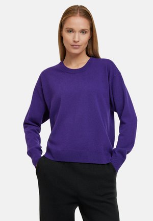 Suéter de punto púrpura con cuello redondo y corte relajado. Cuenta con mangas largas y dobladillo acanalado. Combinado con pantalones negros.