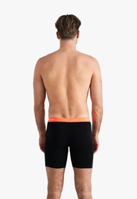 Zwarte boxershorts met een oranje tailleband waarop de tekst "HAPPY SHORTS" staat. De stof lijkt zacht en elastisch.