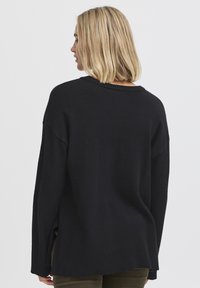 Svart stickad tr�öja med en lös passform, ribbat fåll och vida ärmar. Har en rund halsringning och sidoklipp nertill.