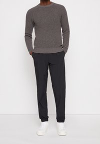 Grauer gerippten Pullover mit langen Ärmeln, kombiniert mit schwarzen leichten Hosen und weißen Turnschuhen, was ein lässiges Outfit ergibt.