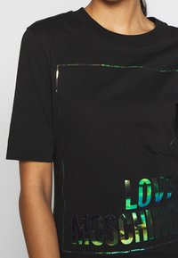 Svart kortärmad t-shirt i bomull med iriserande texten "LOVE MOSCHINO" och en rektangulär foliedesign på framsidan.