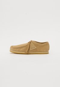Barna nubuk slip-on cipő díszített varrással, látható varratokkal és textúrált gumi talppal. Középen fűzővel ellátva.