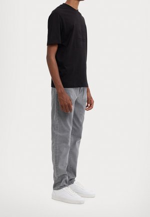 Black short-sleeve t-shirt with a textured logo on the front, paired with light gray jeans and white sneakers, featuring a straight fit.