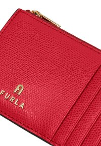 Czerwony skórzany portfel o teksturowanym wykończeniu, z złotymi akcentami i logo Furla. Zawiera wiele przegródek na karty oraz komorę na zamek.