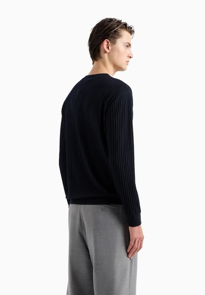 Maglione a coste blu marino realizzato in tessuto testurizzato, con scollatura a girocollo e maniche lunghe, abbinato a pantaloni grigi chiari con dettaglio a bottone.